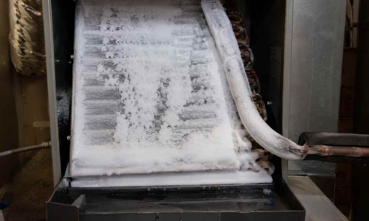 Thick ice and frost covering an evaporator coil and refrigerant line inside a residential air handler, indicating restricted airflow or low refrigerant